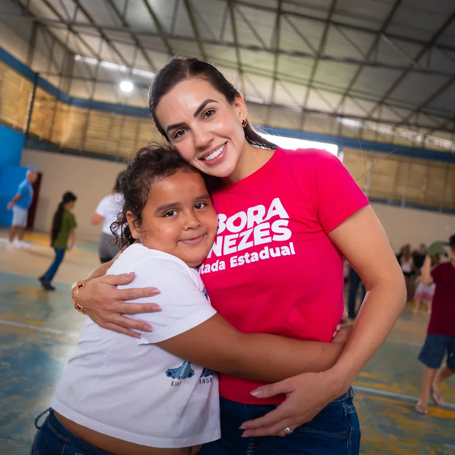 Débora Menezes abraçando uma criança em um ginásio